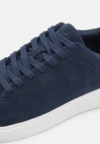 Navyblå mockaskor med en vit gummisula. Har släta snören och en texturerad översida med minimalt med sömmar.