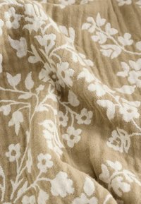 Teflon cu model floral în bej și alb, care prezintă o țesătură moale, texturată, cu modele de flori și frunze vizibile pe întreaga suprafață.
