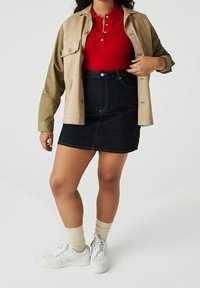 Červené polo tričko pod béžovou bundou, doplněné tmavými džíny sukně. Bílé tenisky a béžové ponožky dotvářejí celkový vzhled.