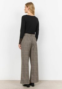 Svart långärmad topp med spetsdetaljer, matchad med vida rutig byxor i brun, beige och svart. Kraftiga klackskor i svart.
