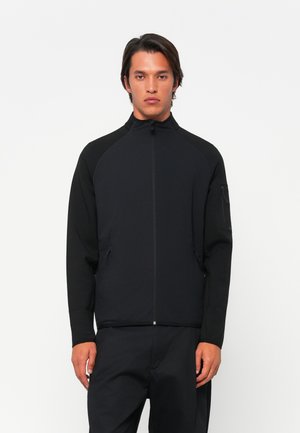 Veste zippée noire avec un col montant, des manches raglan et des poches latérales. Fabriquée en textile texturé avec des accents contrastants sur les épaules.