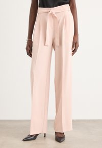Pantaloni palustri rosa chiaro a gamba larga con vita legata, texture liscia e design plissettato. Abbinati a tacchi neri a punta.