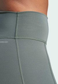 Leggings grigi alti in vita realizzati in tessuto elastico. Presentano cuciture piatte e un logo sottile vicino all'elastico in vita. Texture liscia.
