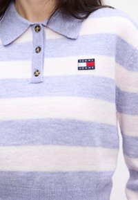 Pulover dungi violet pal și alb, cu guler, având închidere cu nasturi și o aplicație cu logo-ul "Tommy Jeans" pe piept.