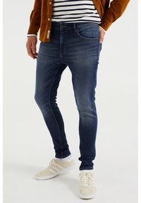 Mörkblå slim-fit jeans med urv washing, i bomullsdenim, klassisk femficksdesign, kombinerade med beige sneakers.