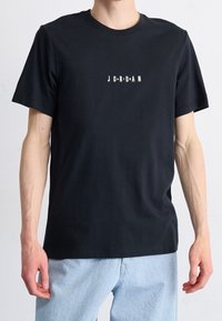 T-shirt in cotone nero con maniche corte e colletto rotondo. Presenta un logo bianco "J O R D A N" stampato sul davanti.