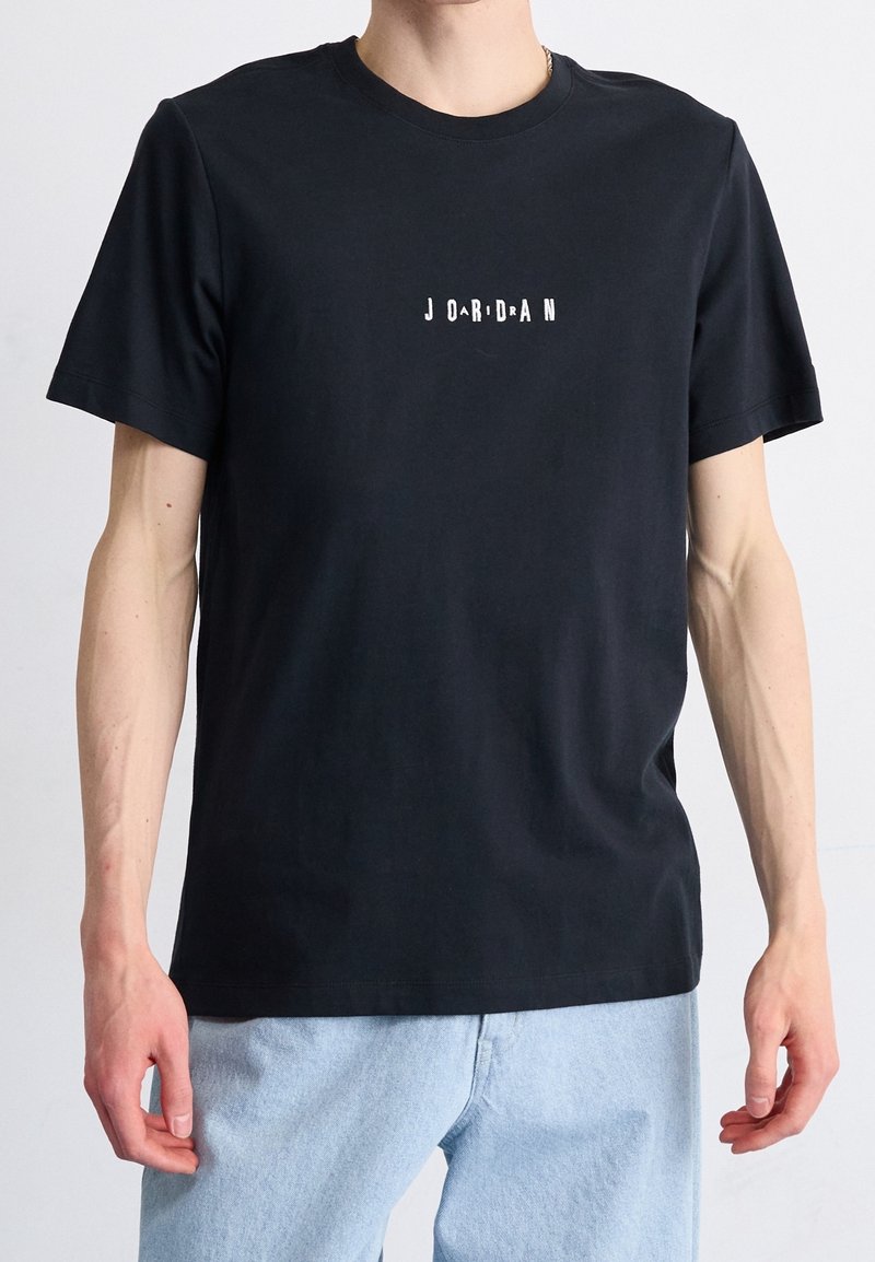 T-shirt in cotone nero con maniche corte e colletto rotondo. Presenta un logo bianco "J O R D A N" stampato sul davanti.