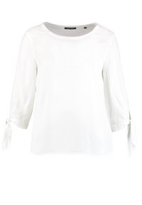 Blouse blanche à manches trois-quarts, avec des accents noués aux manches, un col rond et une texture de tissu lisse.