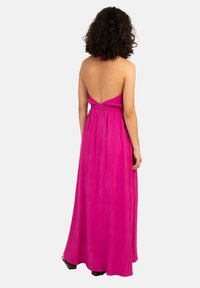 Maxiklänning i livfull rosa med halterneck och öppen ryggdesign. Har textil med struktur och elastik i midjan för en bra passform.