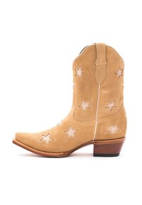 Stivale da cowboy in suede color nocciola con ritagli a forma di stella, punta affusolata e tacco in legno basso. Cuciture decorative lungo i bordi. Chiusura con cerniera sul retro.
