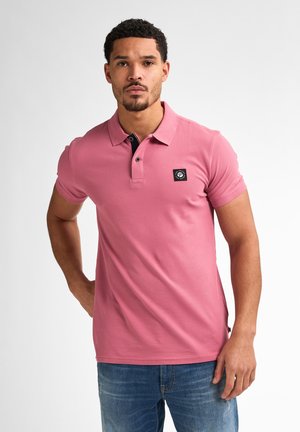 Rosa Polohemd mit schwarzem Kragen, kurzen Ärmeln und einem Logo-Patch auf der Brust. Kombiniert mit blauen Jeans im Slim-Fit-Design.