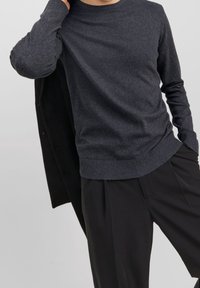 Mörkgrå, stickad tröja med rund halsringning och ribbade ärmslut, kombinerad med svarta byxor. Mjuk textur, minimalistisk design och åtsittande form.