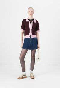 Short-sleeve, burgundy and pink cardigan with buttons, paired with a denim skirt, white socks, patterned sneakers, and a small white handbag.
