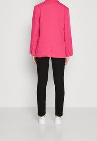 Różowa marynarka z długimi rękawami, wyciętym kołnierzem i rozcięciem z tyłu, zestawiona z czarnymi rurkami i białymi sneakersami. Gładka tekstura.