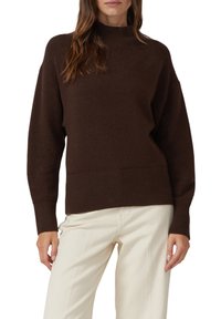 Brauner Strickpullover mit hohem Kragen, gerippten Bündchen und Saum, mit lockerem Sitz und weicher Textur, kombiniert mit hellfarbenen Hosen.