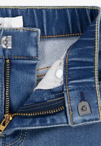 Denim pants with a blue wash, featuring a zip fly with gold hardware, orange stitching, and a soft inner lining.