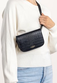Bolsa bandolera de cuero negro con estampado de cocodrilo, diseño con solapa, acento de logo dorado y correa ajustable a juego.