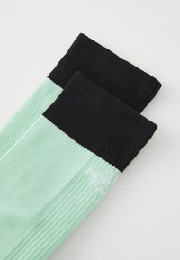 Calcetines de color verde menta y negro con textura acanalada. La sección en menta tiene un logo blanco. El puño negro es liso y contrasta con el color menta.