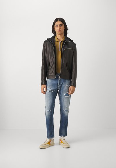 Chaqueta de cuero negro con capucha, cierre frontal y bolsillo lateral. Camiseta polo verde oliva con un pequeño cuello. Vaqueros desgastados de color azul claro. Zapatillas.