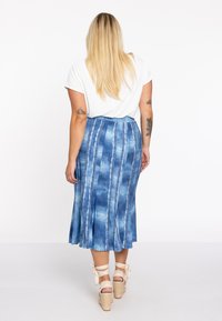 Jupe midi en denim bleu avec des motifs rayés blancs verticaux, une longueur évasée et une taille ajustée. Assortie avec des espadrilles beiges à talons.