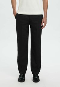 Pantaloni neri su misura con vestibilità dritta, dotati di piega frontale, due tasche laterali e tessuto liscio. Abbinati a mocassini neri.