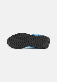 Pantofii sport de culoare albastră, cu o talpă exterioară din cauciuc negru texturat, având un model de șanțuri în zigzag și logo-ul Reebok embosat aproape de toc.