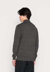 Grijze gebreide pullover met een geribde kraag en manchetten. De stof lijkt zacht met een subtiele textuur. Eenvoudig ontwerp, geen zichtbare patronen.
