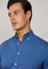 Blauwe overhemdd met een klassieke kraag, voorzien van witte knopen en een klein geborduurd logo op de borst. Glad, textuurstof.