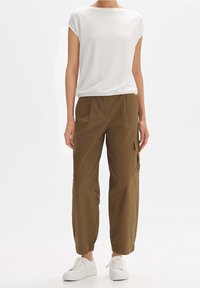 Top bianco a maniche corte, vestibilità comoda, abbinato a pantaloni cargo verde oliva con polsini elastici e tasche laterali, indossato con sneakers bianche.