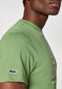 Πράσινο βαμβακερό t-shirt με στρογγυλή λαιμόκοψη, που διαθέτει μικρό κεντημένο λογότυπο κροκ οδείλου στο αριστερό μανίκι και λεία υφή.