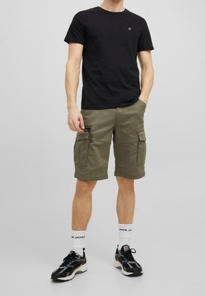 Schwarzes Baumwoll-T-Shirt, olivgrüne Cargo-Shorts mit Utility-Taschen, kombiniert mit schwarz-weißen Sneakern und weißen Socken.