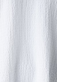 Tessuto bianco dal texture con un sottile motivo a pantina, morbido al tatto, con un aspetto leggero e arioso e un colore uniforme e tenue.
