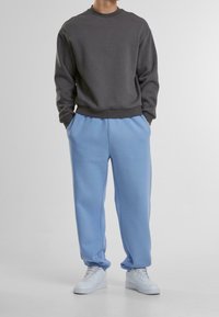Dunkelgrauer Pullover mit Rundhalsausschnitt, kombiniert mit hellblauen Jogginghosen mit elastischem Bund und seitlichen Taschen. Getragen mit weißen Turnschuhen.