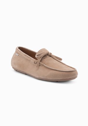 Zapato mocasín de ante color marrón claro con punta redondeada, cordones y suela de goma. Presenta una costura a lo largo de los bordes.