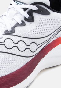 Λευκό αθλητικό παπούτσι με μαύρα κορδόνια, μαύρο και κυκλικό λογότυπο, επάνω μέρος από διαπνέον πλέγμα και κόκκινη και λευκή μαλακή σόλα.