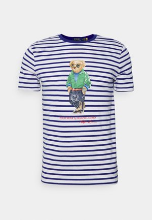 T-shirt blanc pour homme avec des rayures horizontales bleu marine et un graphique central représentant un ours portant des lunettes de soleil, une veste verte et un pantalon rayé.