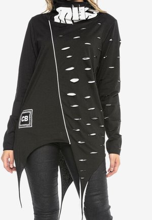 Czarny asymetryczny top z długim rękawem z białym napisem na kołnierzu, z rozdartym wzorem z jednej strony, białą pionową linią i naszywką przy szwie, noszony z czarnymi spodniami.