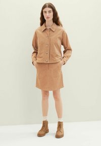 Veste en velours côtelé marron clair avec deux poches avant, fermetures à boutons, associée à une jupe assortie et des bottes à lacets marron.