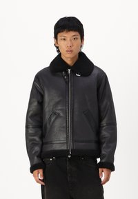 Schwarze, mit Schaffell gefütterte Lederjacke mit weitem Kragen, Reißverschluss und zwei Fronttaschen. Verfügt über eine strukturierte Oberfläche und kontrastierenden Wollbesatz.