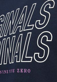 Mėlynas medvilnės marškinėliai su dideliu baltu užrašu "ORIGINALS" ir "NINE NINE ZERO" rožine spalva. Minkšta tekstūra, apvaliu kaklu ir trumpomis rankovėmis.