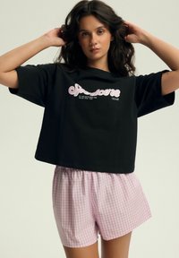 Czarna przycięta koszulka z różowym nadrukiem; zestawiona z jasnoróżowymi szortami w białą kratkę. Wygodny bawełnowy materiał, luźny krój.