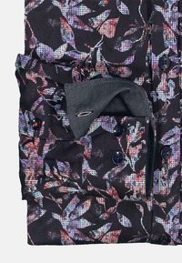 Blusenshirt mit floralem Muster, schwarzem Hintergrund, lila und roten Akzenten, Knopfleiste und einem abgesetzten grauen Manschetten, die eingesteckt ist.