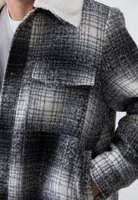 Giacca a scacchi in bianco e nero realizzata in tessuto testurizzato, con colletto in shearling e tasche anteriori per maggiore dettaglio e funzionalità.