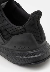 Shoe desportivo preto com um upper em malha texturizada, sola de borracha e logótipo distintivo da tecnologia de amortecimento Boost no calcanhar.