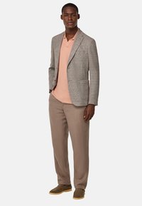 Grå strukturerad kavaj över en ljusrosa polo, kombinerad med beige byxor och bruna skor. Ensemblet har en skräddarsydd passform utan synliga mönster.