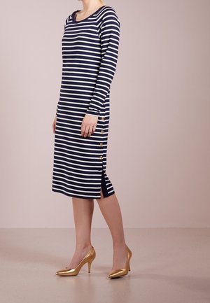 Robe à manches longues rayée bleu marine et blanche avec un décolleté en scoop et des détails de boutons sur le côté, assortie à des chaussures à talons hauts dorées.