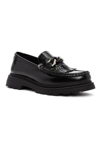 Mocasines de cuero negro con un diseño texturizado, que presentan un acento decorativo con flecos y una suela de goma gruesa para mayor agarre.
