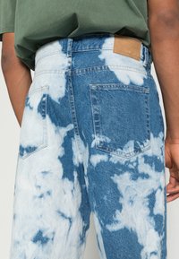 Light blue tie-dye denim jeans with a high waist, back pockets, and a tan leather label at the waistband. Textured cotton fabric.