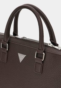 Braune, strukturierte Lederhandtasche mit zwei Tragegriffen, silbernem Beschlägen und einem Reißverschlussverschluss. Mit einem dreieckigen Metalllogo auf der Vorderseite.