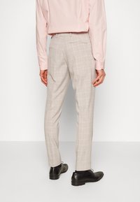 Bežové kárované nohavice so slim fit strihom vyrobené z ľahkej tkaniny, ktoré majú vrecká a elegantný vzhľad v kombinácii s čiernymi formálnymi topánkami.